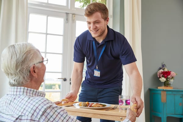 Staff serving a meal to a resident in a bright room