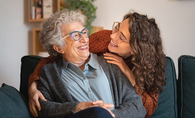 A senior woman and a younger woman smiling together on a couch