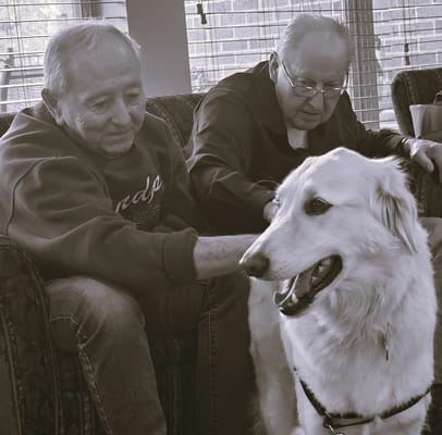 Two residents interacting with a dog in a cozy lounge area