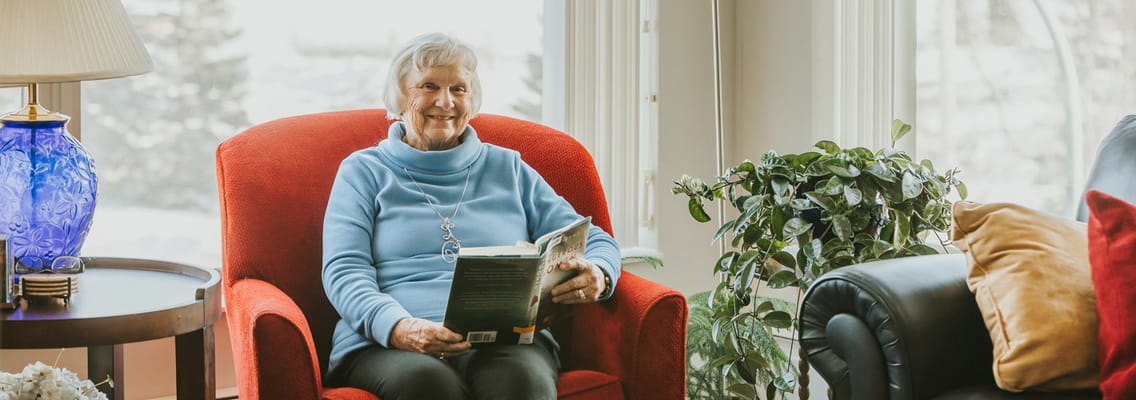 A resident reading in a cozy chair by a window