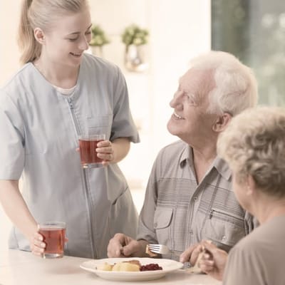 Caregiver serving food to residents in a dining room