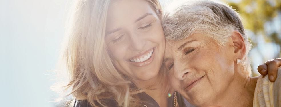 A caregiver embraces a senior woman outside.