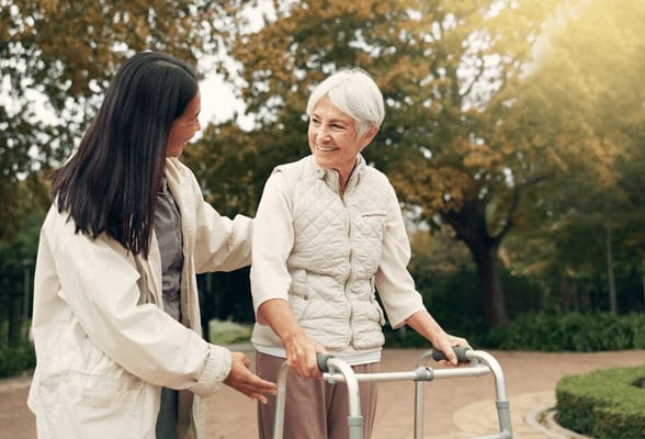 Senior resident using a walker in a garden with staff assistance