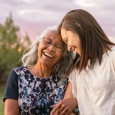 Two women joyfully laughing outdoors in a garden
