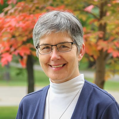 A smiling woman in front of colorful trees