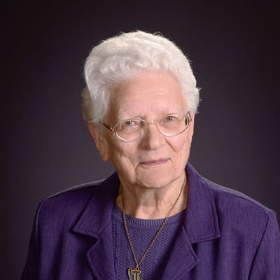 A senior woman with glasses wearing a purple blazer