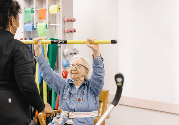 An elderly woman exercising with staff assistance
