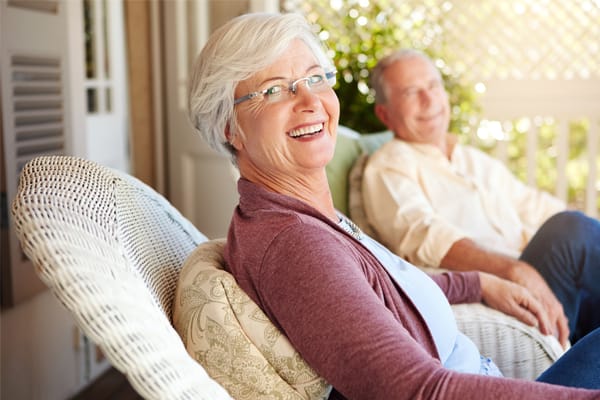Smiling senior woman outdoors with a man in background