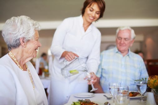 Waitstaff serving food to residents in a dining room