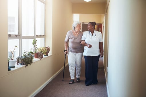 A staff member assisting an elderly resident in a hallway