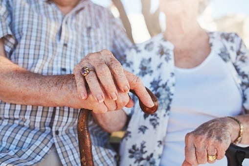 Two seniors holding hands on a bench