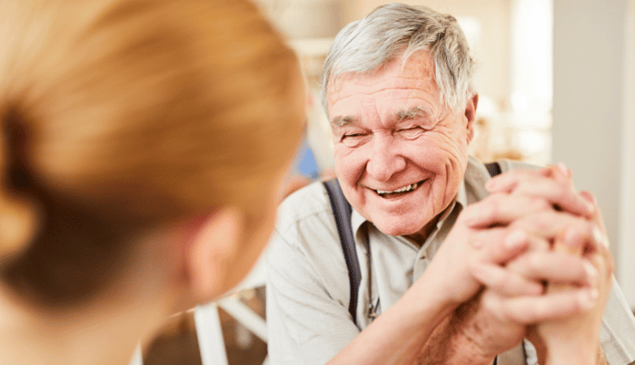 An elderly man smiling and holding hands with a caregiver