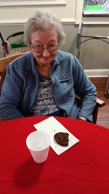 A smiling elderly resident enjoying a cookie at a table