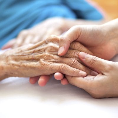 Close-up of a caregiver holding an elderly person's hand