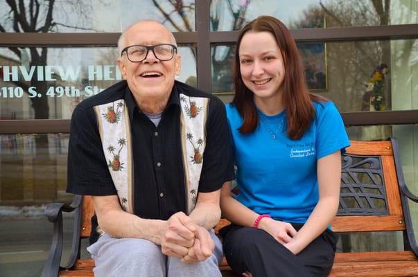 A resident and staff member smiling on a bench outside