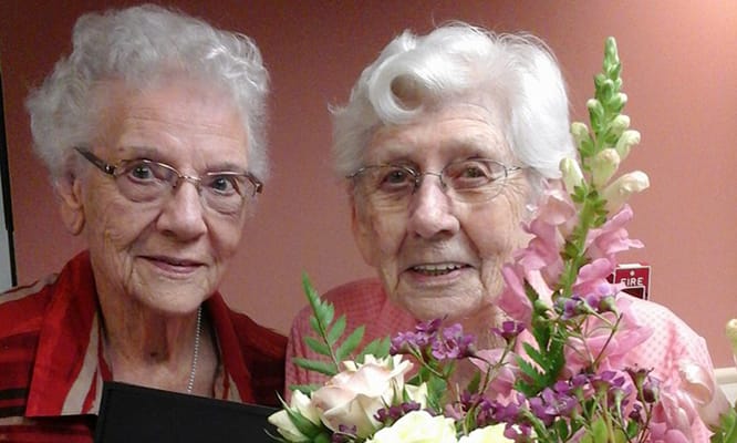 Two smiling residents holding flowers in a bright activity room