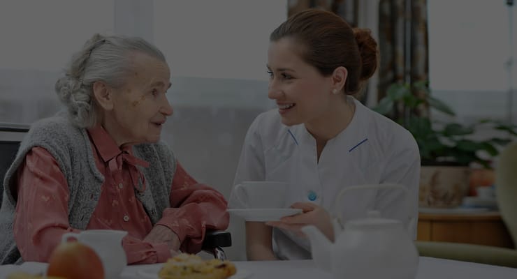 A caregiver serving tea to a senior resident in a cozy setting