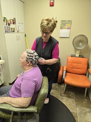 Staff member setting rollers in resident's hair in salon area