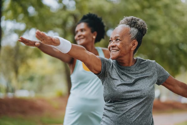 Two older women exercising outdoors with smiles