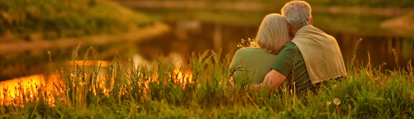 Elderly couple embracing by a serene lake at sunset