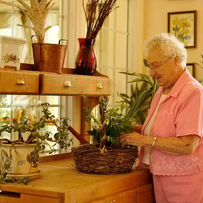An elderly woman tending to indoor plants