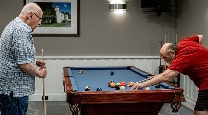 Two residents playing pool in an activity room.