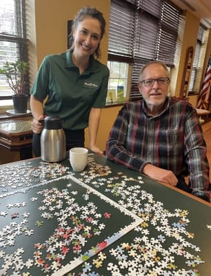 A staff member serving coffee to a resident while working on a puzzle