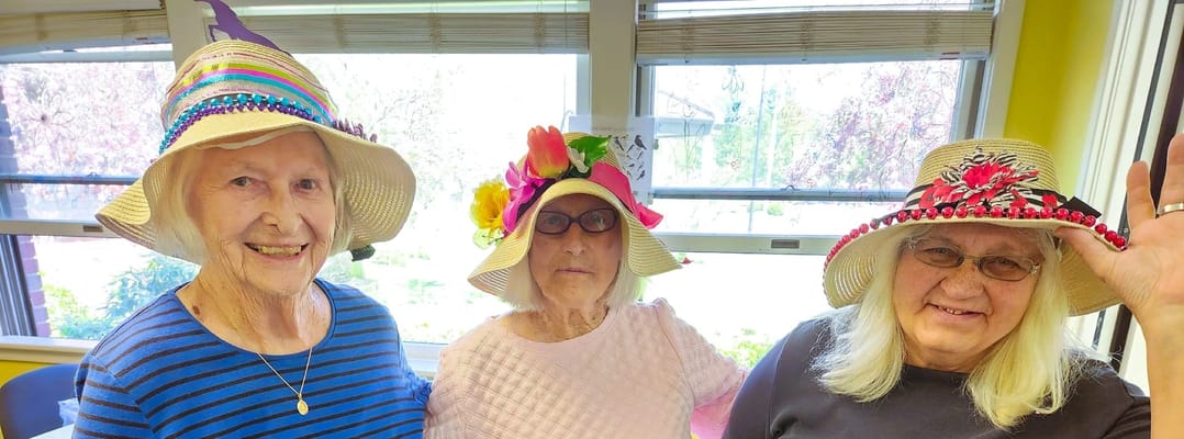 Three residents smiling in colorful hats inside a facility