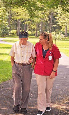 A staff member helping an elderly resident walk outside