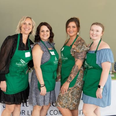 Staff members in green aprons smiling at an event