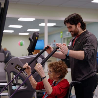 Senior resident exercising with staff assistance in a fitness room