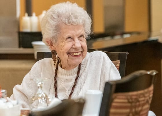 Elderly woman smiling while seated at a dining table