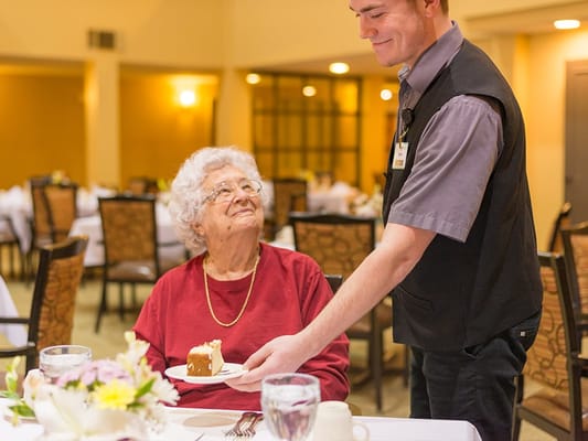 A staff member serving cake to an elderly resident in the dining room