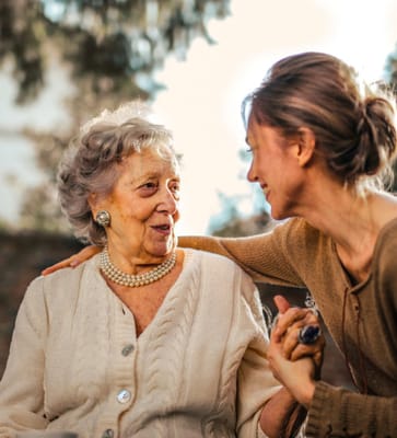 An older woman and a caregiver smiling together outdoors