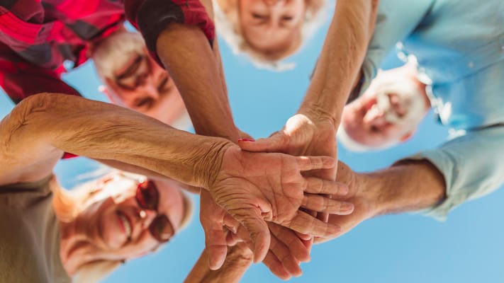 Group of seniors smiling and stacking their hands together outdoors
