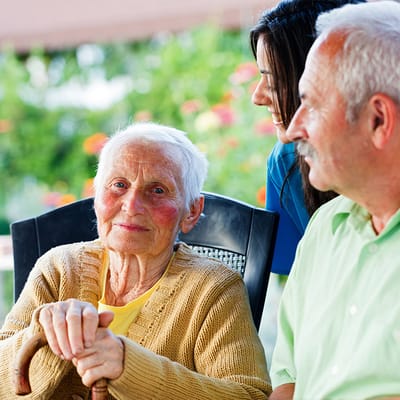 A senior resident smiling with staff in a garden setting