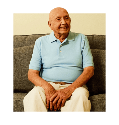 An elderly man smiling while sitting on a couch