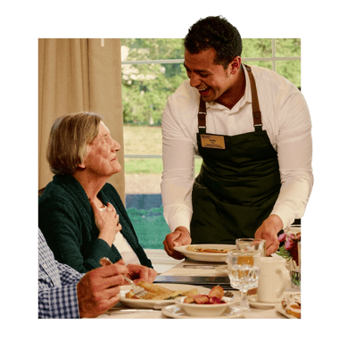 Staff serving a meal to a resident in a dining area