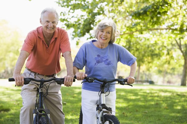 Two seniors smiling on bicycles in a park