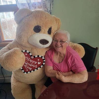 A resident smiling with a large teddy bear on Valentine's Day