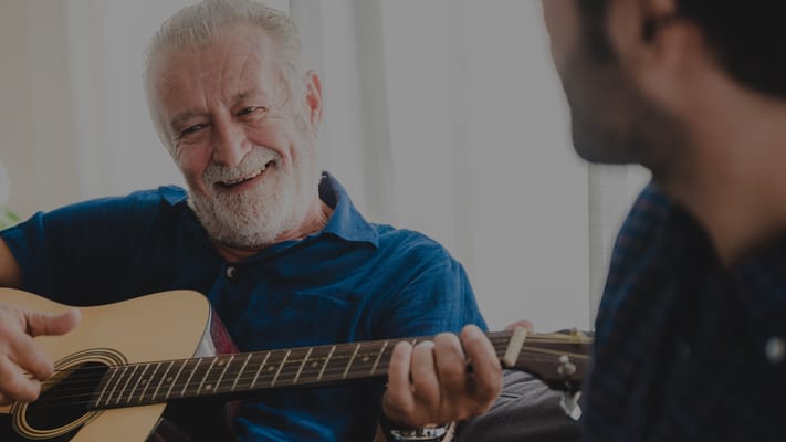 Senior man playing guitar and interacting with a caregiver