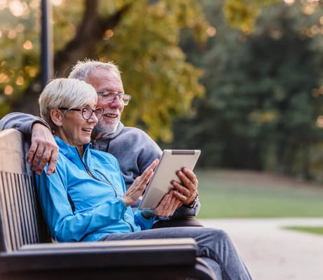 Two seniors enjoying a tablet on a park bench