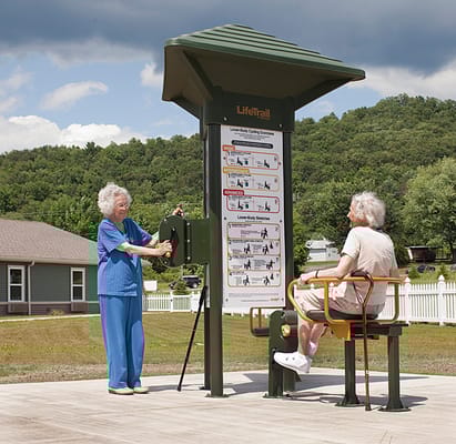 Residents using outdoor exercise equipment in a park-like setting