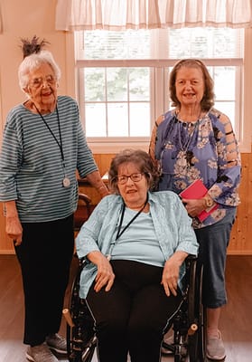 Three residents posing in a sunny activity room