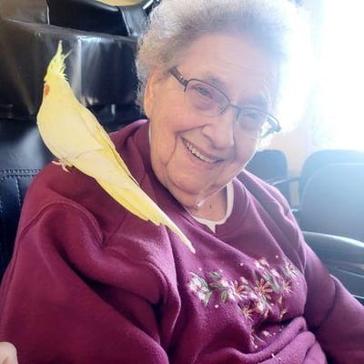 Resident smiling with a cockatiel perched on her shoulder