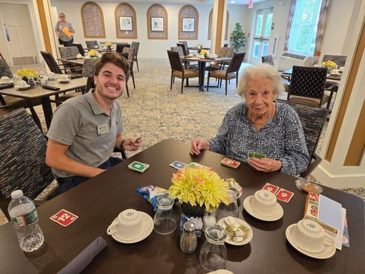 A resident playing cards with staff in a dining room