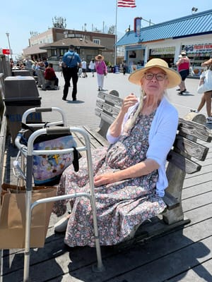A woman sitting on a bench outdoors with a walker