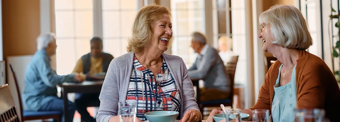 Residents enjoying a meal and laughing in the dining area