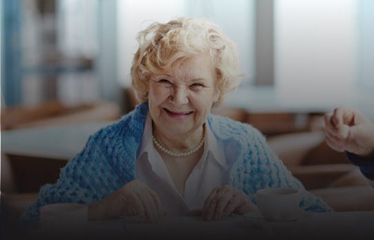 An elderly woman smiling in a dining area