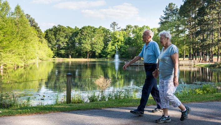 Two seniors walking by a serene pond in a park
